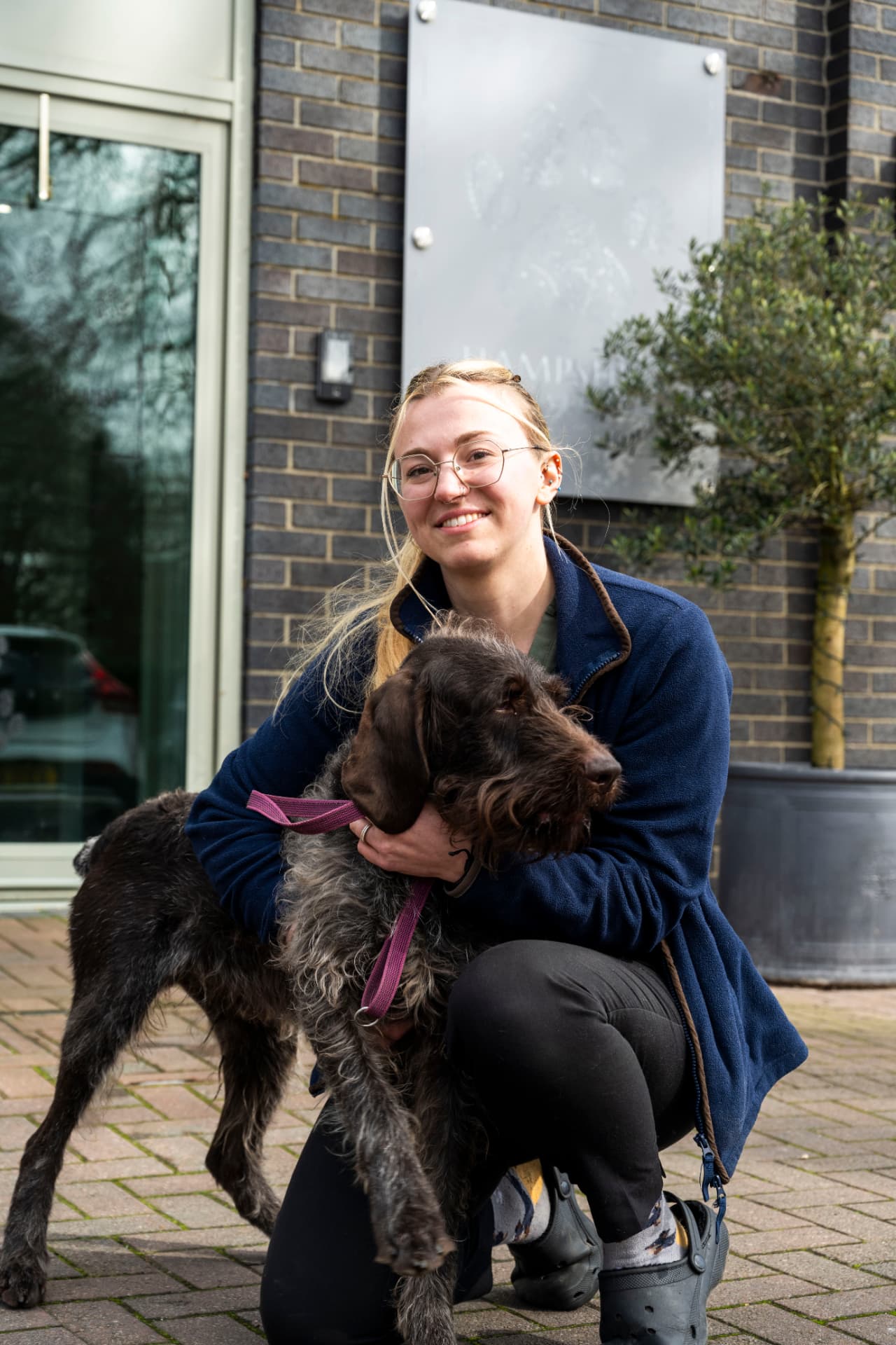 Team member outside a veterinary practice holding a large wire-haired dog